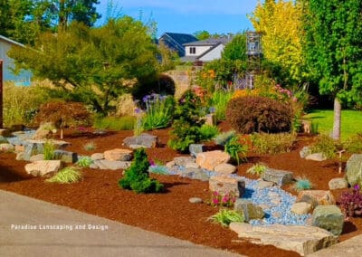 Front yard landscape with bushes and rocks.